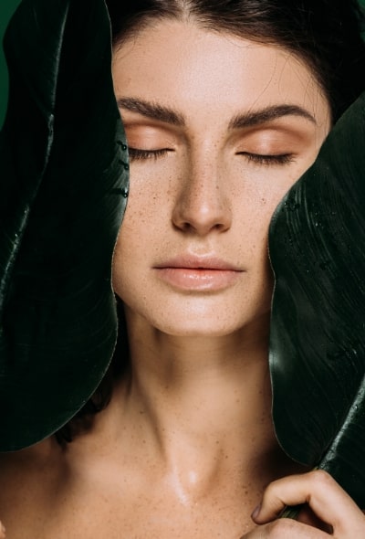 Eine brünette Frau mit geschlossenen Augen und einem grünen Blatt in der Hand